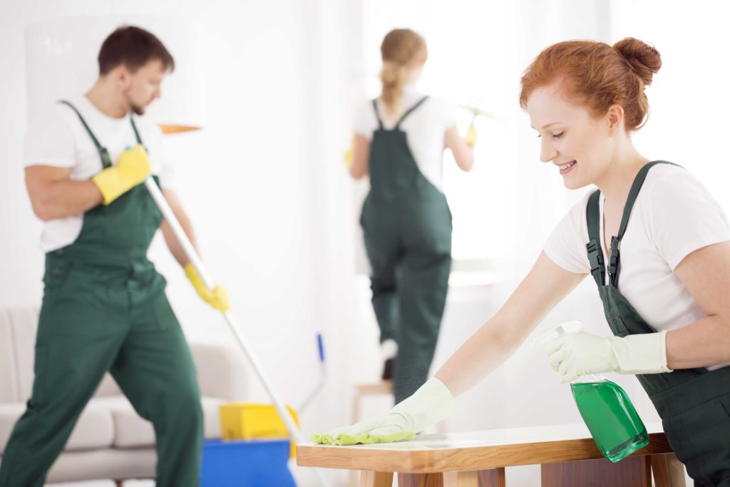 Group of cleaners in white shirts and green overalls