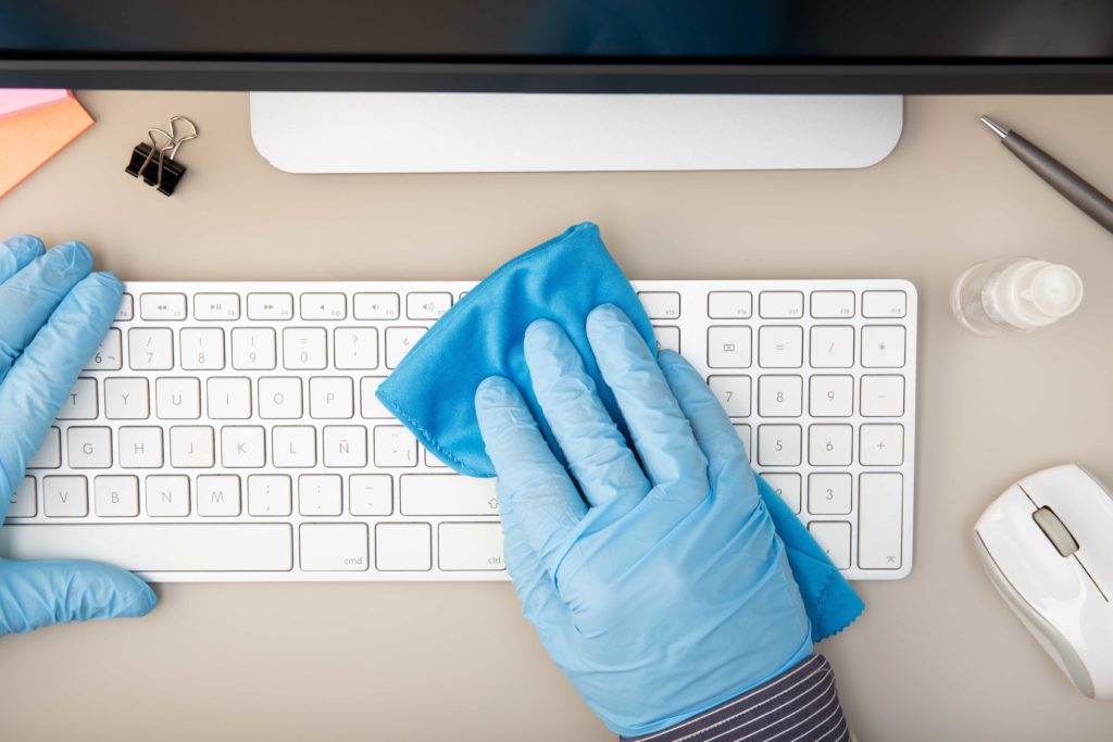 Hands in blue gloves wiping keyboard
