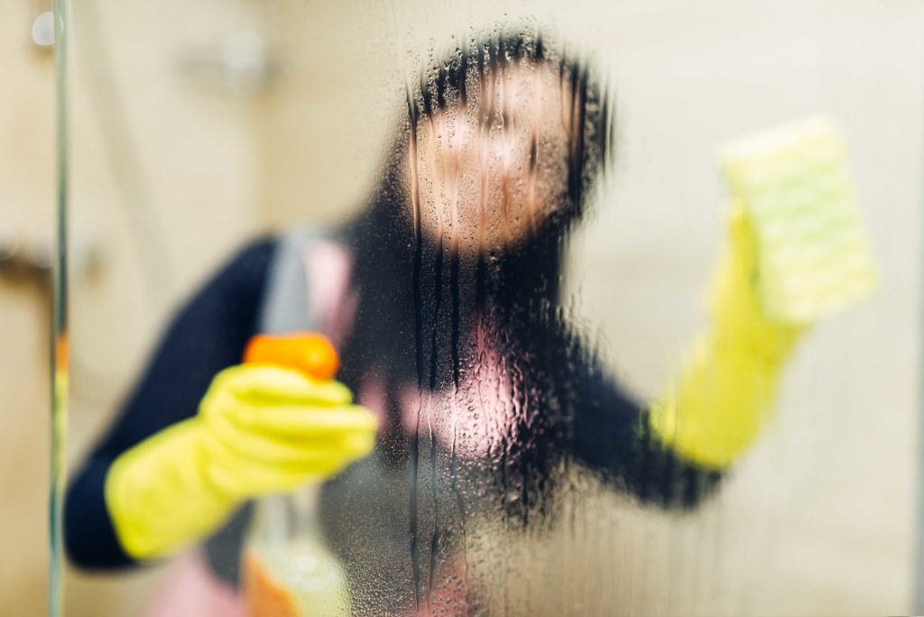 Woman behind shower glass while cleaning it